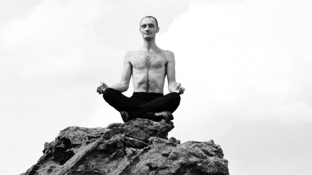 Shirtless man meditates cross-legged atop a rock in La Capelle-et-Masmolène, France.